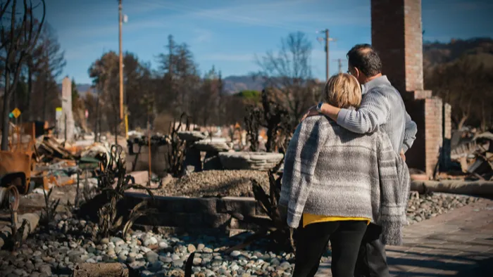 A couple holding each other as they look over the burned ruins of their neighborhood