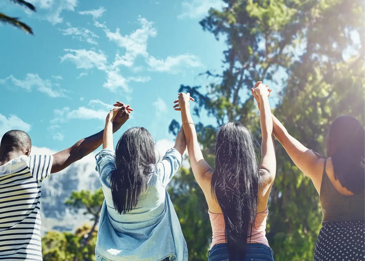 A group of friends raising their joined hands outdoors under the trees